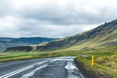 Empty road leading towards mountains against cloudy sky