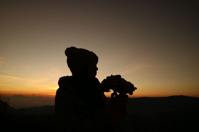 Silhouette boy holding orange against sky during sunset