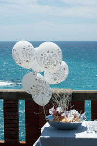 Balloon decoration on table by sea against sky