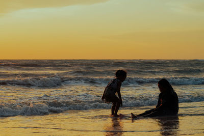 Silhouette of children sitting by the beach during golden sunset.