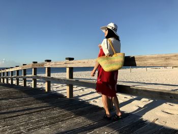 Woman standing by railing at beach against sky