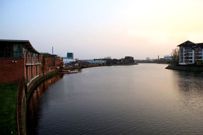 Buildings by river against sky during sunset