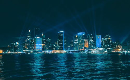 Illuminated buildings by sea in city at night