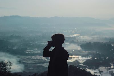 Silhouette man looking at cityscape against sky