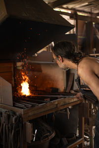 Blacksmith stoking the fire in the forge of his workshop.	
