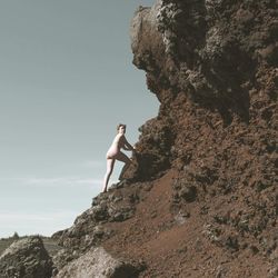 Low angle view of woman standing on rock against sky