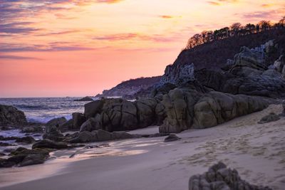 Rocks on beach against sky during sunset