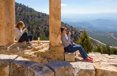 Young couple sitting on mountain against sky