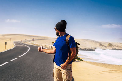 Man gesturing while standing on empty road against sky