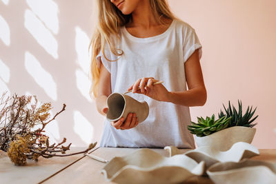 Midsection of woman holding earthenware on table at home