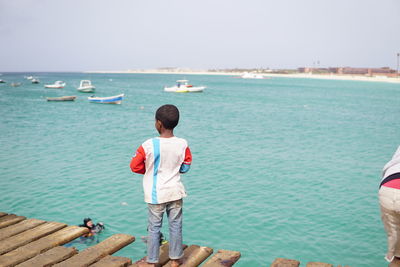 Rear view of boy standing on pier over sea against sky