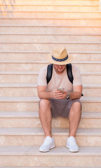 Middle-aged bearded man wearing sunhat using cellphone,mobile,texting, chatting, sitting at stairs