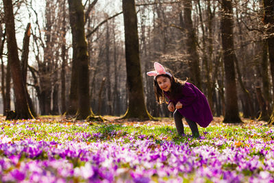 Woman with pink flowers on field by trees in forest