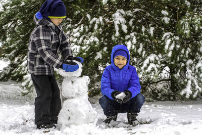 Portrait of boy with brother making snowman during winter