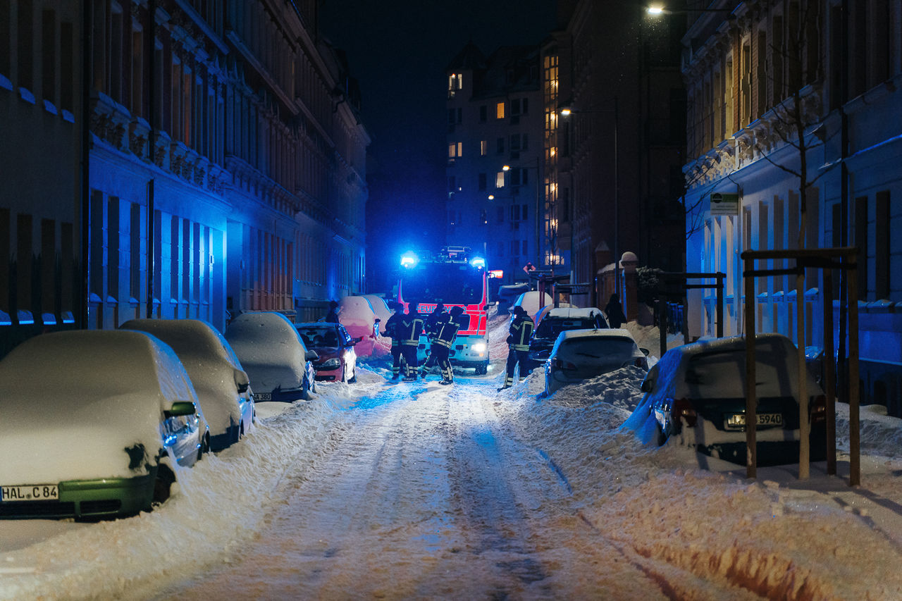 snow, night, winter, illuminated, architecture, city, transportation, cold temperature, street, mode of transportation, building exterior, urban area, car, built structure, vehicle, motor vehicle, blue, nature, evening, light, travel, city street, lighting