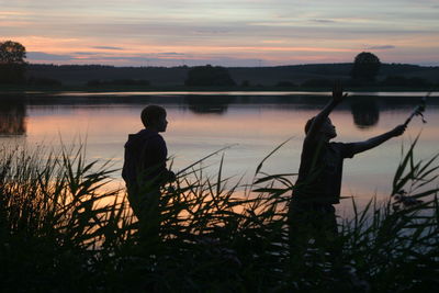 Silhouette man standing by lake against sky during sunset