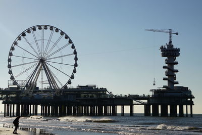 Ferris wheel by sea against clear sky