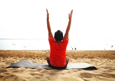 Rear view of woman practicing yoga at beach against clear sky