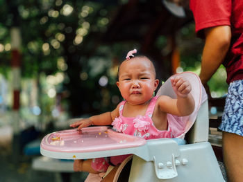 Portrait of cute baby girl crying while sitting on high chair in yard