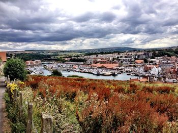 High angle view of town by river against cloudy sky