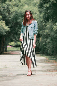 Portrait of beautiful woman standing on footpath amidst trees in park