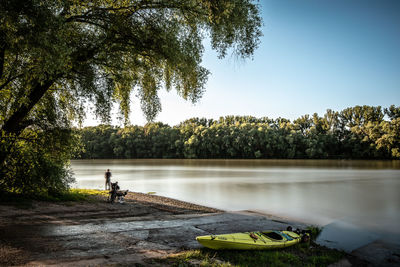 Man sitting by lake against clear sky