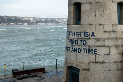 Information sign by sea against sky