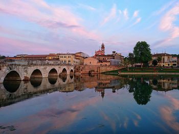 Arch bridge over river by buildings against sky