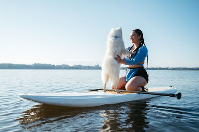 Happy young woman hugging with her dog japanese spitz while sitting on the sup board