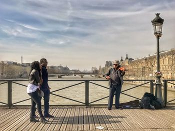 People on railing in city against cloudy sky