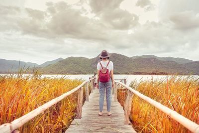 Rear view of a woman standing on railing against sky