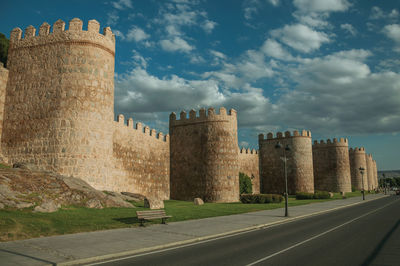 Street and light posts beside stone towers in the large wall encircling the town of avila, in spain.