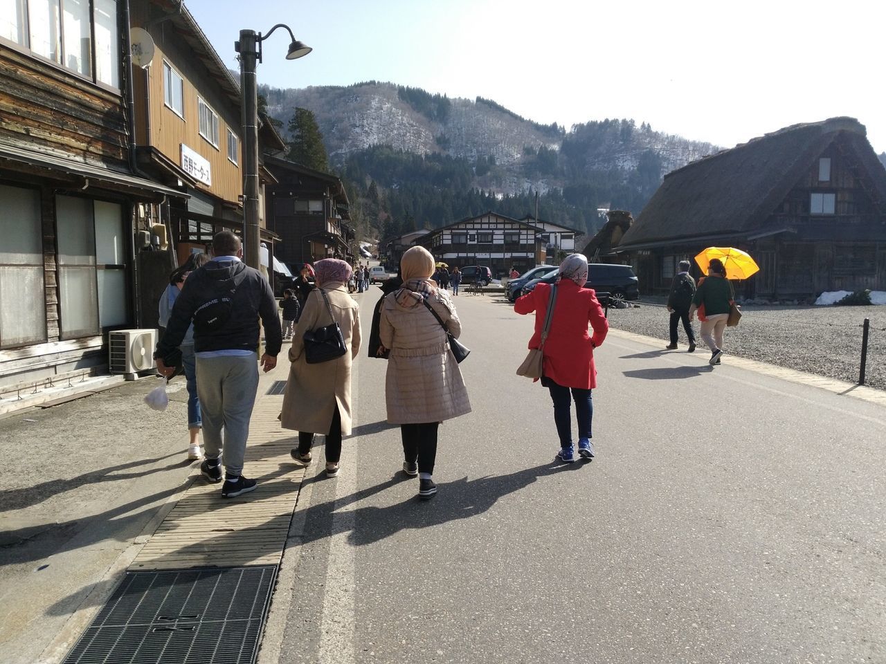 REAR VIEW OF PEOPLE WALKING ON STREET AGAINST BUILDINGS