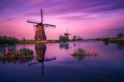 Traditional windmill by lake against sky during sunset