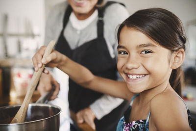 Portrait of happy girl cooking food with grandmother in kitchen