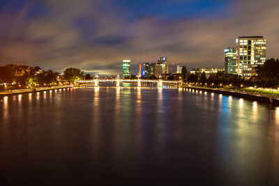 Illuminated buildings by river against sky in city at night