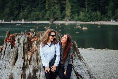 Mother and daughter leaning on large tree stump by lake