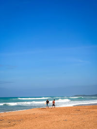 Surfers standing at beach against clear blue sky