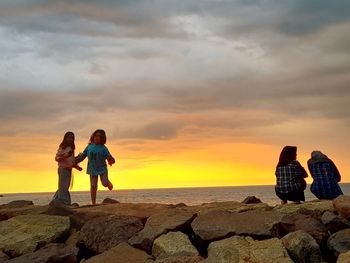 Women on rocks by sea against sky during sunset