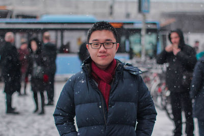 Portrait of smiling young man wearing warm clothing in city during snowfall