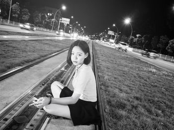 Full length portrait of young woman sitting in city at night