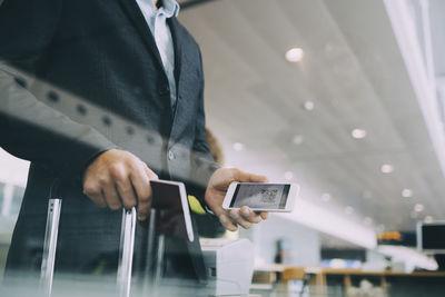 Midsection of mid adult businessman holding passport and smart phone at airport