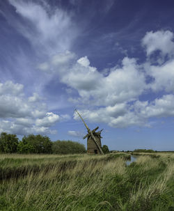 Old damaged windmill on grassy field against sky