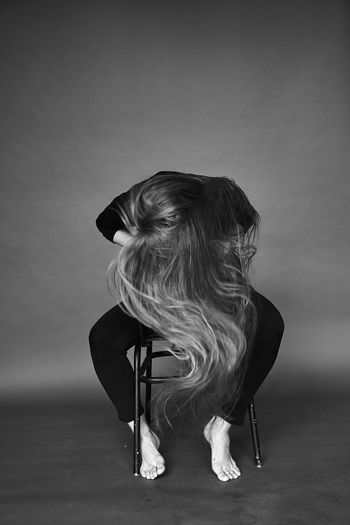 Woman covering her face by hair while sitting on chair against gray background