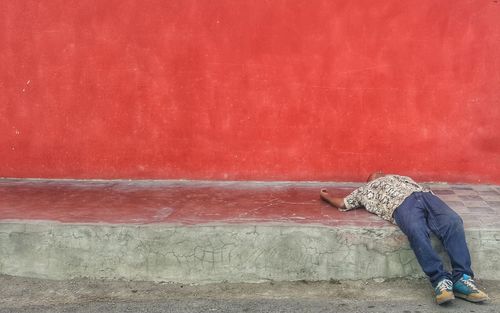 Side view of woman sitting against red wall