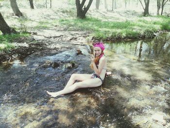 High angle view of young woman wearing bikini sitting in lake at forest