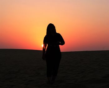 Rear view of silhouette man standing on beach during sunset
