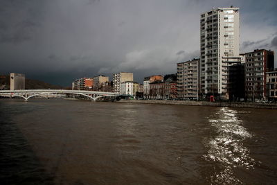 Bridge over river by buildings against sky in city