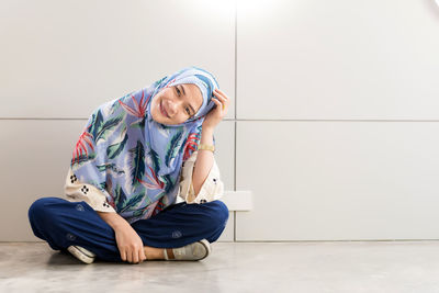 Portrait of smiling young woman wearing hijab sitting on tiled floor