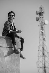 Young man wearing sunglasses while sitting on wall against sky